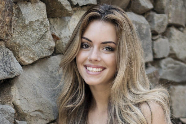 Lächelnde junge blonde Frau vor Natursteinmauer